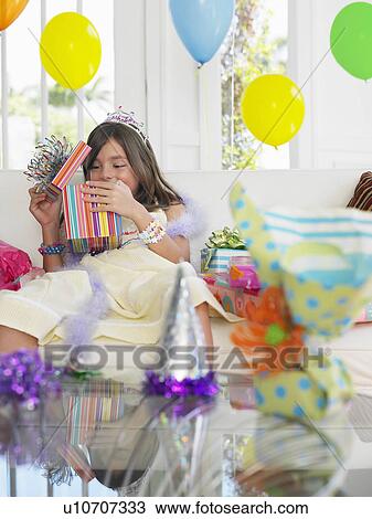 Stock Image - Young girl (7-9) opening birthday presents. Fotosearch