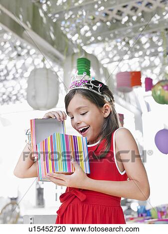 Stock Image - Young girl (7-9) opening birthday present at party. Fotosearch