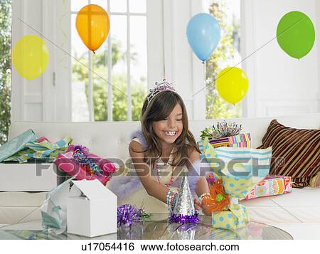 Stock Photograph - Young girl (7-9) opening birthday presents smiling. Fotosearch