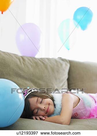 Stock Photo - Young girl (7-9) sleeping on sofa with balloons. Fotosearch