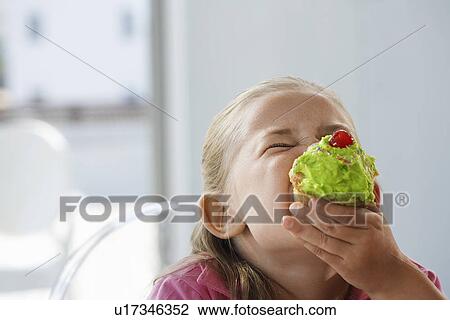 Stock Image - Young girl eating cupcake head and shoulders. Fotosearch