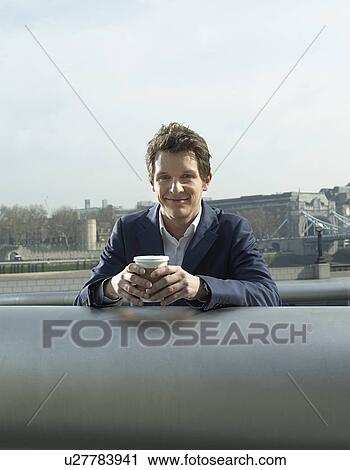 Young man in suit leaning on pipe outdoors drinking coffee View Large Photo Image Stock Image - Young man in suit leaning on pipe outdoors drinking coffee. Fotosearch
