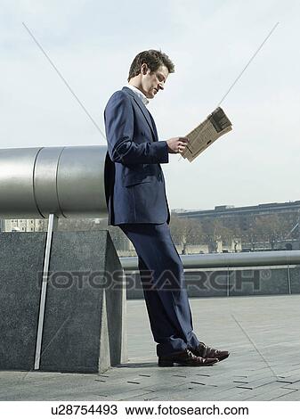 Young man in suit leaning on pipe outdoors reading paper side view View Large Photo Image Stock Image - Young man in suit leaning on pipe outdoors reading paper side view. Fotosearch