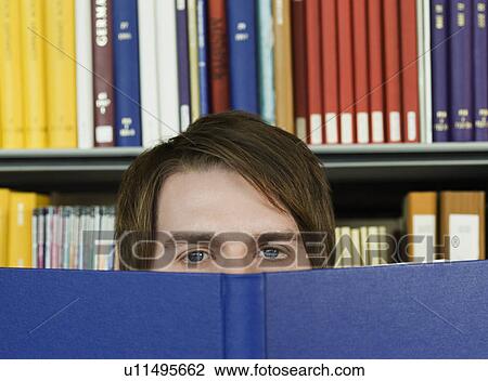 Stock Image - Young man peeking over opened book. Fotosearch