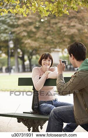 Young man photographing young woman on bench in park View Large Photo Image Stock Image - Young man photographing young woman on bench in park. Fotosearch