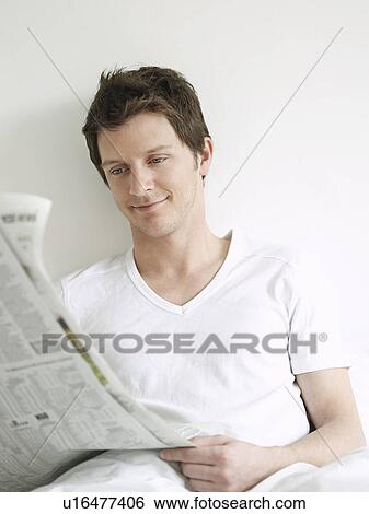 Young man reading newspaper in bed and smiling View Large Photo Image Stock Photograph - Young man reading newspaper in bed and smiling. Fotosearch