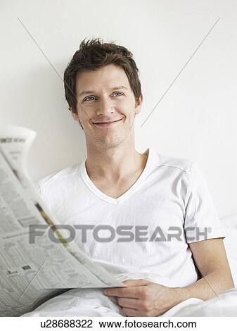Young man reading newspaper in bed looking to side and smiling View Large Photo Image Stock Image - Young man reading newspaper in bed looking to side and smiling. Fotosearch