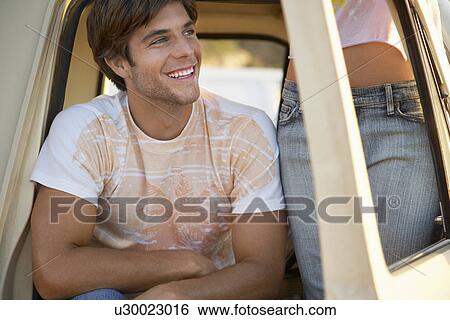 Stock Photograph - Young man sitting in van doorway young woman standing mid section. Fotosearch