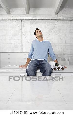 Stock Image - Young man sitting on desk looking up. Fotosearch