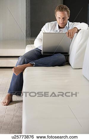 Young man sitting on sofa using laptop portrait View Large Photo Image Stock Photograph - Young man sitting on sofa using laptop portrait. Fotosearch