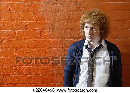 Stock Photograph - Young man standing in front of orange brick wall. Fotosearch