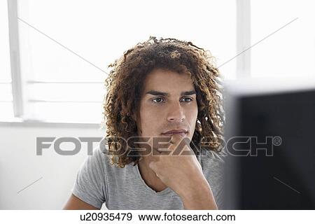 Young man using computer sitting at desk View Large Photo Image Stock Photo - Young man using computer sitting at desk. Fotosearch