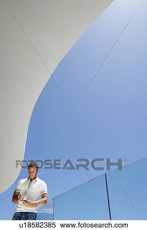 Young man using mobile phone on balcony portrait low angle view View Large Photo Image Stock Photography - Young man using mobile phone on balcony portrait low angle view. Fotosearch
