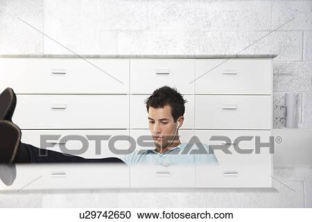 Stock Image - Young man wearing earphones legs on table top. Fotosearch