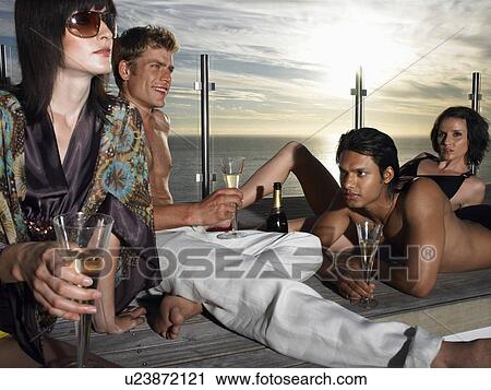 Stock Image - Young people drinking champagne on pool deck near sea at sunset. Fotosearch