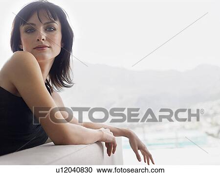 Stock Image - Young woman leaning on couch indoors. Fotosearch