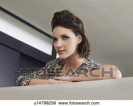 Young woman leaning on couch indoors View Large Photo Image Stock Photo - Young woman leaning on couch indoors. Fotosearch