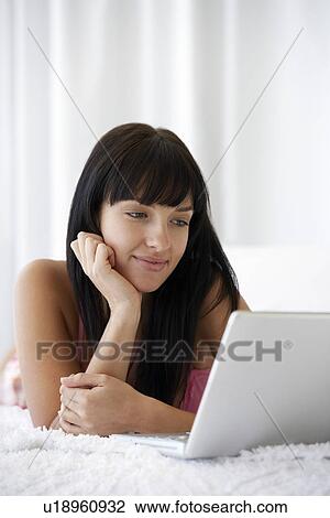 Young woman lying on bed using laptop portrait View Large Photo Image Stock Image - Young woman lying on bed using laptop portrait. Fotosearch