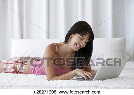 Young woman lying on bed using laptop portrait View Large Photo Image Stock Photo - Young woman lying on bed using laptop portrait. Fotosearch