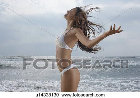 Stock Image - Young woman on beach enjoying breeze profile. Fotosearch