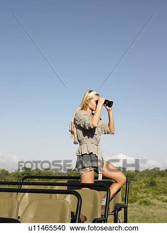 Young woman on safari standing in jeep looking through binoculars side view View Large Photo Image Stock Image - Young woman on safari standing in jeep looking through binoculars side view. Fotosearch