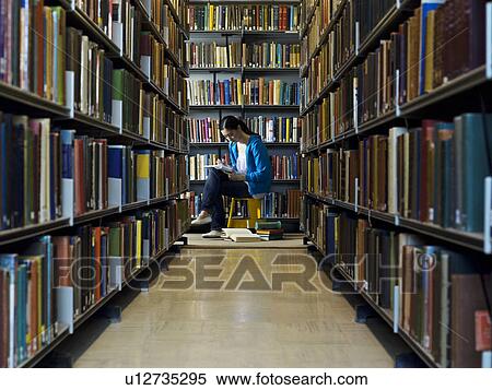 Stock Photography - Young woman reading by bookshelf in library. Fotosearch