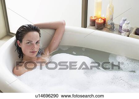 Stock Image - Young woman relaxing in bubble bath elevated view. Fotosearch