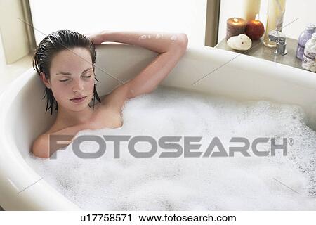 Stock Image - Young woman relaxing in bubble bath eyes closed. elevated view. Fotosearch