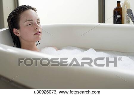 Stock Image - Young woman relaxing in bubble bath eyes closed. Fotosearch