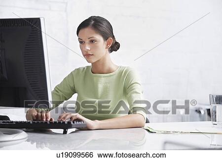 Stock Photograph - Young woman sitting at desk using computer. Fotosearch