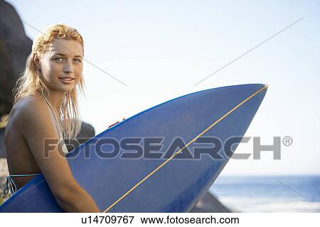 Young woman sitting by rocks holding surfboard View Large Photo Image Stock Photo - Young woman sitting by rocks holding surfboard. Fotosearch