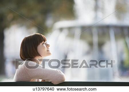 Young woman sitting on bench in front of fountain head and shoulders View Large Photo Image Stock Image - Young woman sitting on bench in front of fountain head and shoulders. Fotosearch