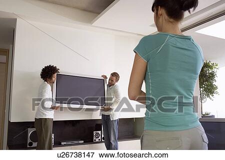 Young woman watching as two young men move plasma television back view View Large Photo Image Stock Photo - Young woman watching as two young men move plasma television back view. Fotosearch