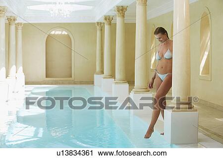 Stock Image - Young woman wearing bikini stepping into swimming pool. Fotosearch