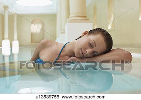 Stock Photograph - Young woman with eyes closed leaning on edge of swimming pool portrait. Fotosearch