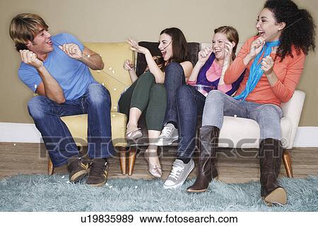 Stock Photo - Young women throwing popcorn at friend on sofa. Fotosearch