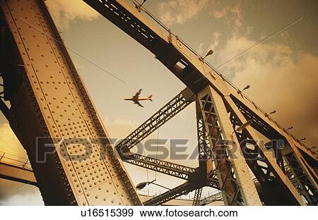Stock Photo - Airbourne passenger jet viewed through bridge superstructure. Fotosearch
