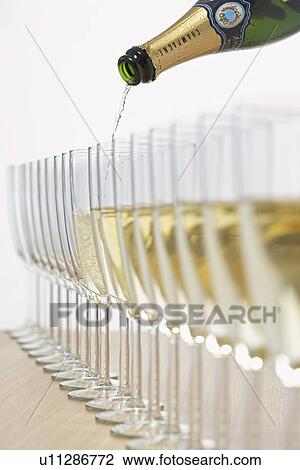 Stock Image - Bottle of champagne filling row of glasses selective focus. Fotosearch