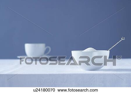 Stock Image - Bowl of sugar on table tea cup in background. Fotosearch