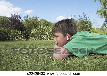 Boy (10-12) lying on elbows in grass listening to mp3 player View Large Photo Image Stock Image - Boy (10-12) lying on elbows in grass listening to mp3 player. Fotosearch