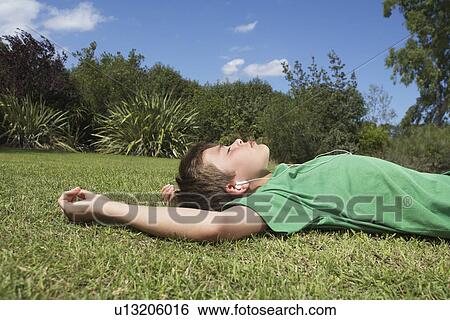 Boy (10-12) lying on grass listening to mp3 player View Large Photo Image Stock Photograph - Boy (10-12) lying on grass listening to mp3 player. Fotosearch