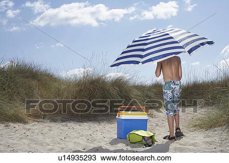 Boy (10-12) standing on beach under umbrella back view View Large Photo Image Stock Image - Boy (10-12) standing on beach under umbrella back view. Fotosearch