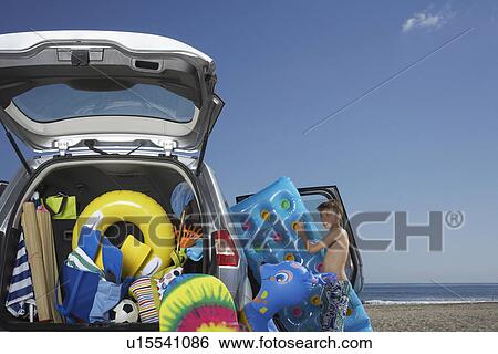Boy (10-12) unloading air mattress from car full of beach accessories View Large Photo Image Stock Photograph - Boy (10-12) unloading air mattress from car full of beach accessories. Fotosearch