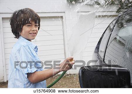 Stock Photo - Boy (7-9) washing car with hose. Fotosearch