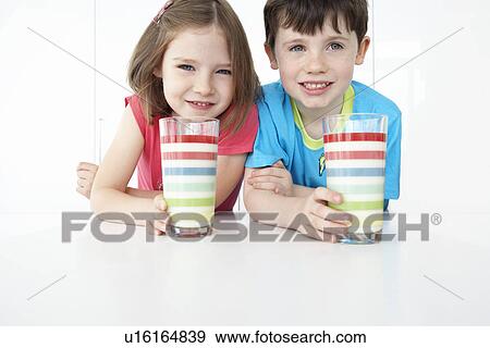 Stock Photo - Boy and girl (5-6) sitting at table holding colourful glasses portrait. Fotosearch