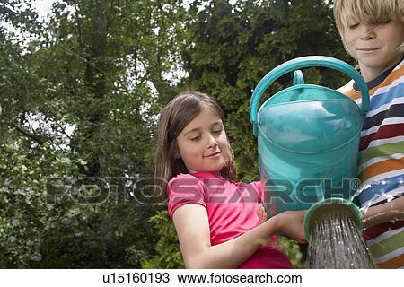 Stock Image - Boy and girl (7-9) watering garden together. Fotosearch