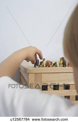 Picture - Boy arranging dinosaurs figurines close-up back view. Fotosearch