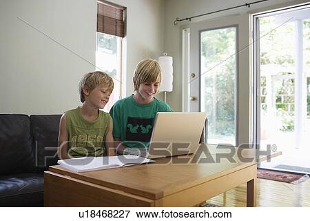 Brothers (6-11) sitting at table using laptop smiling View Large Photo Image Stock Photo - Brothers (6-11) sitting at table using laptop smiling. Fotosearch