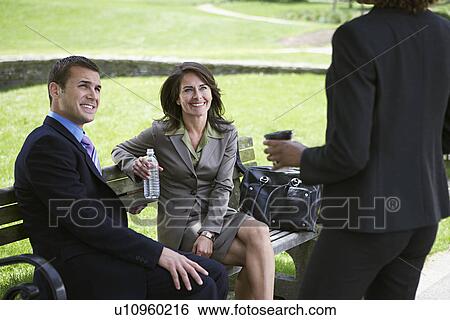 Business man and woman sitting on park bench looking at colleague View Large Photo Image Stock Photograph - Business man and woman sitting on park bench looking at colleague. Fotosearch