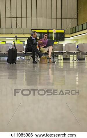 Stock Photograph - Business man and woman using laptop in airport lobby. Fotosearch